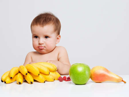 Baby boy indoor portrait with fruits on the table. Healthy eating concept.の写真素材