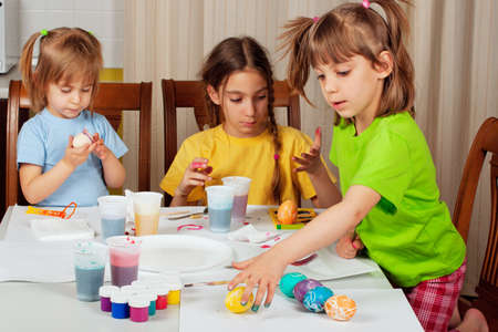 Three little girls (sisters) painting on Easter eggs at home kitchenの写真素材