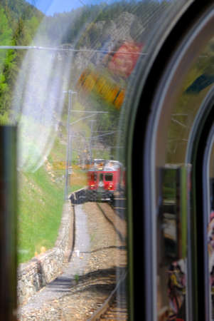 The red Bernina train coming, seen through the passenger window during a sunny dayの写真素材