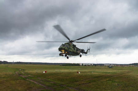 Military helicopter takes off from a grass field in the background of the cityの写真素材