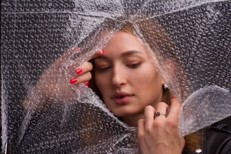Abstract mysterious portrait girl hidden behind breaking plastic wrap in black background and...