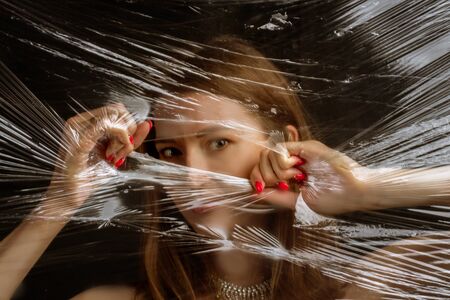 Abstract mysterious portrait girl hidden white behind breaking stretch cellophane and looking...