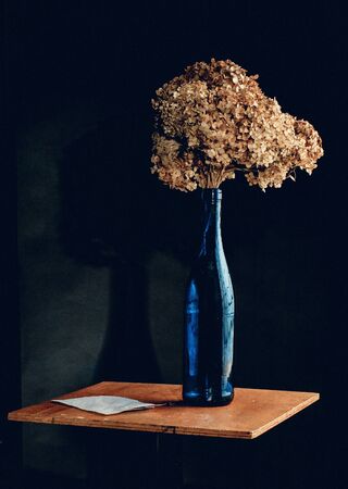 still life with a blue bottle, dry flowers and a piece of paper on a dark backgroundの写真素材