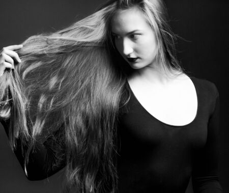 portrait of a girl holding in hand-shows off her long blonde hair on a dark background black and whiteの写真素材