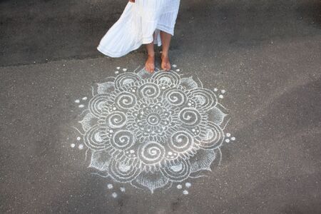 the girl's bare feet and the hem of a white dress on the background of asphalt with a chalk patternの写真素材