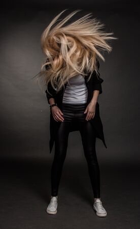 dynamic Studio shot of a blonde girl on a dark background with hair flying to the sides