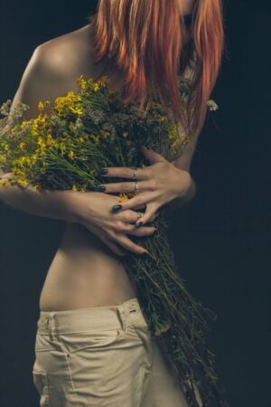 Studio portrait of a girl on a dark background without a face with a bouquet of flowers.の写真素材