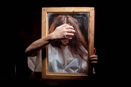 A mystical and frightening Studio portrait of a girl looking through a frame. Hands with outstretched fingers in front.の写真素材