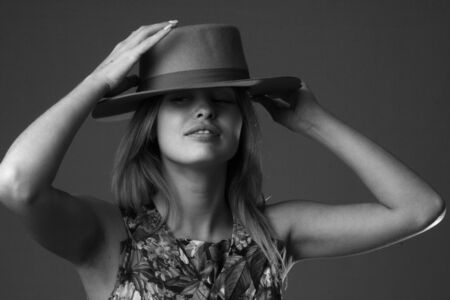 black and white Studio portrait of a girl in a hat and dress on a black background. The girl hides her face under the shadow of her hat.の写真素材