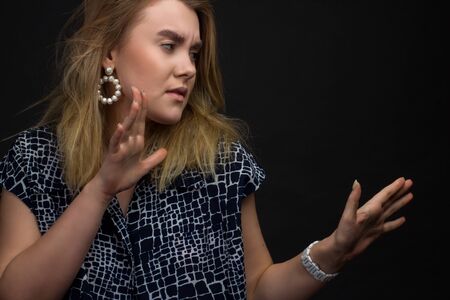 portrait of blonde girl on a dark Studio background, hands and the face of expresses discontent,...