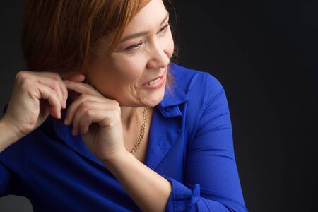 Studio portrait of an attractive woman on a dark background with a short haircut Oriental type fastens the earringの写真素材