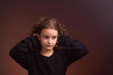 Studio portrait of a little girl with long curly hair in a black fluffy jacket and a pink skirt...