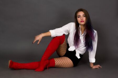 Girl brunette in a white shirt and red boots and stockings in a large mesh sitting on a gray studio...