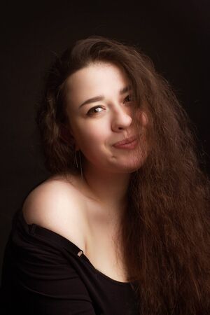 Studio portrait of a brunette with long curly hair on a dark background in a black t-shirtの写真素材