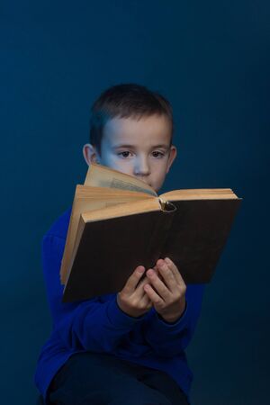 Studio portrait of a boy on a blue background in a classic t-shirt. Holding a book and readsの写真素材