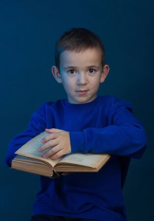 Studio portrait of a boy on a blue background in a classic t-shirt. Holding a book. turns the pagesの写真素材