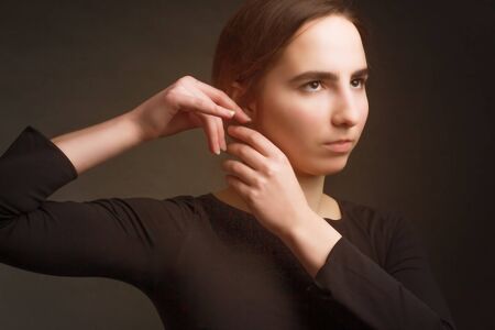 The brown-haired girl in dark clothes, a portrait on a dark gray Studio background. Warm toning....