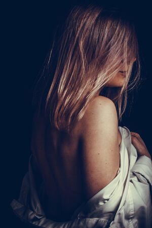 portrait of a blond girl wrapped in a white shirt Studio photo on a dark gray background. turned back, head in profile. dark in tone, dramatic lightingの写真素材