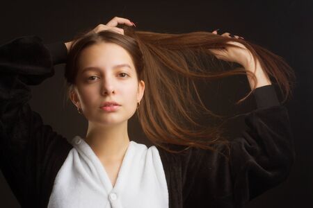 portrait of a brunette girl in the Studio on a plain black background in black and white pajamas with a hood, pulling her hair over her head with her handsの写真素材