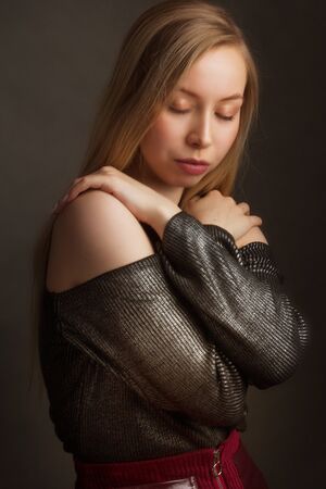 portrait of a blonde in the Studio on a dark uniform background in a black shiny blouse with open shoulders and a red and maroon skirt. closed eyes and hands crossed on his chestの写真素材