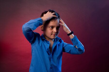 The Studio portrait of boy is a brunette, in a blue shirt on a purple and maroon background. holding...
