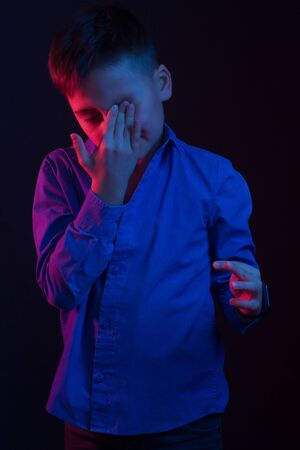 Studio portrait of a dark-haired boy, on a dark background, in a hoodie jacket in the hood. light color: red and blueの写真素材