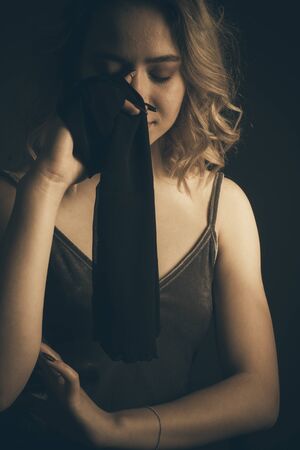 Studio portrait of a blonde on a dark background in a dark dress he closes his eyes with a black ribbonの写真素材