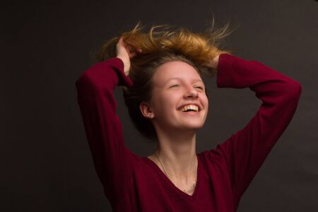 portrait of a girl in the Studio with painted blonde hair, in a red sweater. Warm toned. hands on the headの写真素材