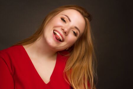 a blonde girl with an overweight plus size, in a red overall posing on a dark Studio background.