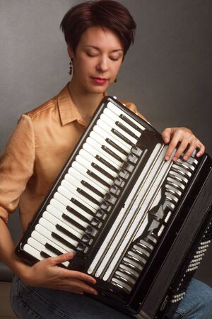 A brunette in a gold shirt, with a short haircut, on a light gray background of the Studio. With accordion musicianの写真素材