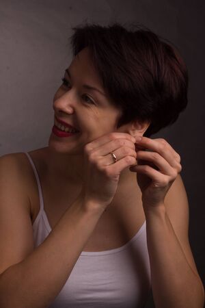 brunette with short hair. Studio portrait in white t-shirt. fingers pulls the earlobeの写真素材