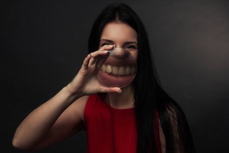 portrait of a brunette on gray studio background in a red dress, smile and Holding Magnifying Glass...