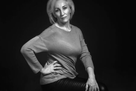 Classic black-and-white dramatic portrait of an elderly blonde woman in Studio on black background....