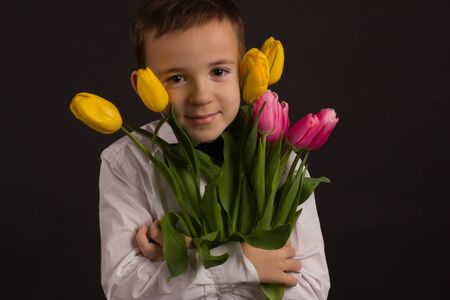 the boy with vitiligo in white shirt and a bow tie with tulips on a black Studio backgroundの写真素材