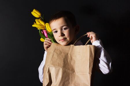 the boy with vitiligo in a white shirt and a bow tie with tulips on a black Studio background