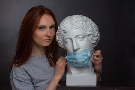 ginger young woman girl on a black background a gray t-shirt and plaster bust in protective medical...