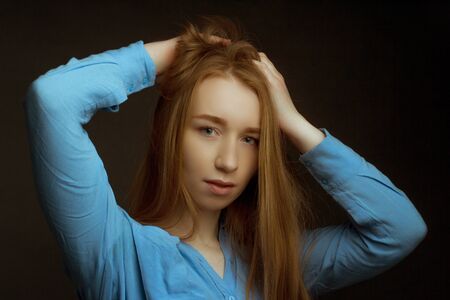 portrait of girl young woman with long blonde hair wearing a blue shirt. straightens hair. A dark...