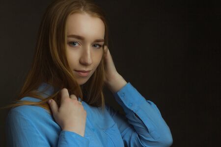 portrait of girl young woman with long blonde hair wearing a blue shirt. straightens hair. A dark image.の写真素材