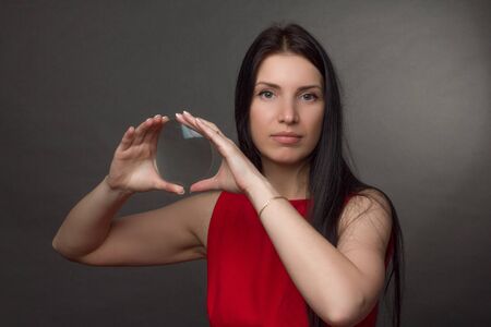 Portrait of a brunette in a red dress. looks through a magnifying glassの写真素材
