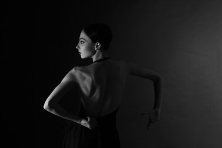monochrome vintage dramatic portrait of a girl in the Studio on gray background. view from the back, a ballerina dancing and gesticulatingの写真素材