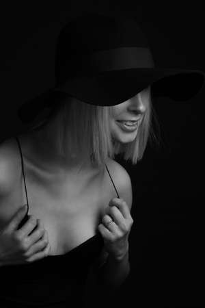 Black and white portrait blondes on a black background in a hat and Tank Top With Thin Straps. laughing, holding hands on clothesの写真素材