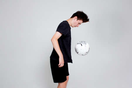 A young man in a black sports t-shirt and shorts, training and playing with a soccer ball. Isolated on white.の写真素材
