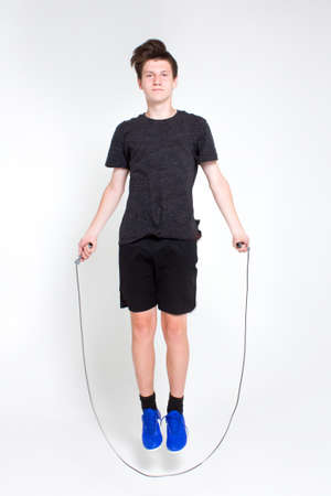 A young boy in a black sports t-shirt and shorts, blue sneakers, practicing jumping rope