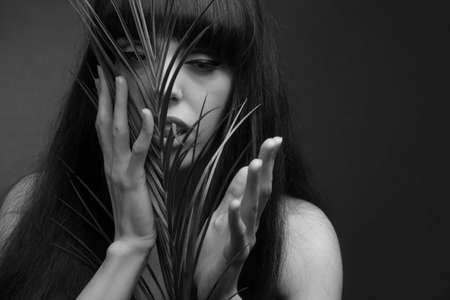 black and white portrait of brunette with long hair, off shoulder, holding a palm leaf
