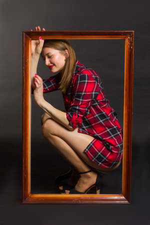 Studio photo of a young woman with long brown hair in a red checked shirt and bare legs