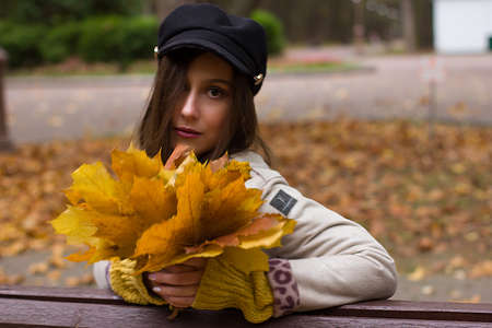 Portrait of a young woman with brown hair, wearing a black cap and a white coat. Against the background of an autumn Park.の写真素材