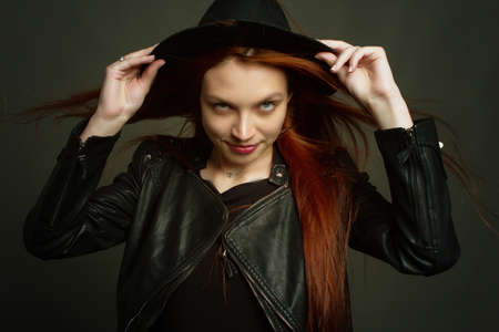 portrait of a young red-haired woman in a black dress and. Studio photo on a black background.