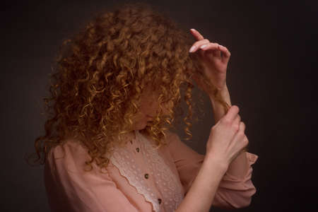 Studio portrait of a young woman with curly hair. Plays with a lock of hair. The concept of care and the health of the hairの写真素材