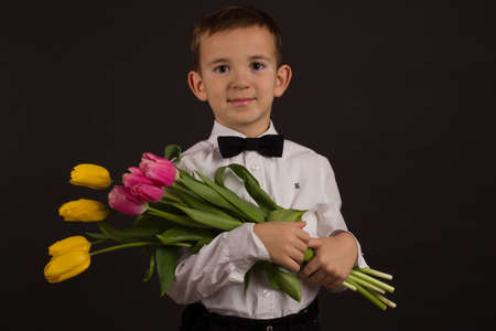 the boy with vitiligo in a white shirt and a bow tie with tulips on a black Studio backgroundの写真素材