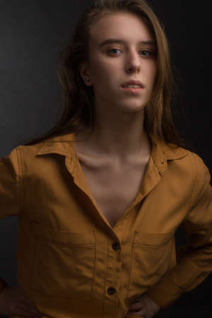 portrait of a young beautiful woman in a studio in dark colors, in a yellow shirtの写真素材